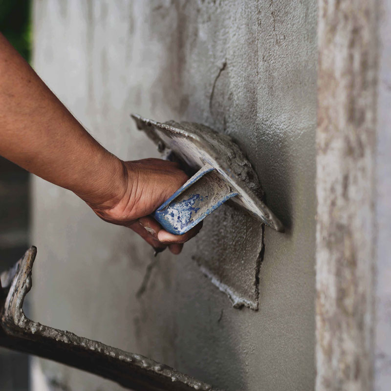 Ein Handwerker trägt frischen Putz auf eine Wand auf und glättet die Oberfläche mit einer Kelle. Die Nahaufnahme zeigt die geübte Handführung, das Werkzeug sowie die noch feuchte, strukturierte Putzschicht. Die Szene vermittelt präzises Arbeiten im handwerklichen Innenausbau und zeigt den sorgfältigen Verarbeitungsvorgang bei Putz- oder Sanierungsarbeiten.